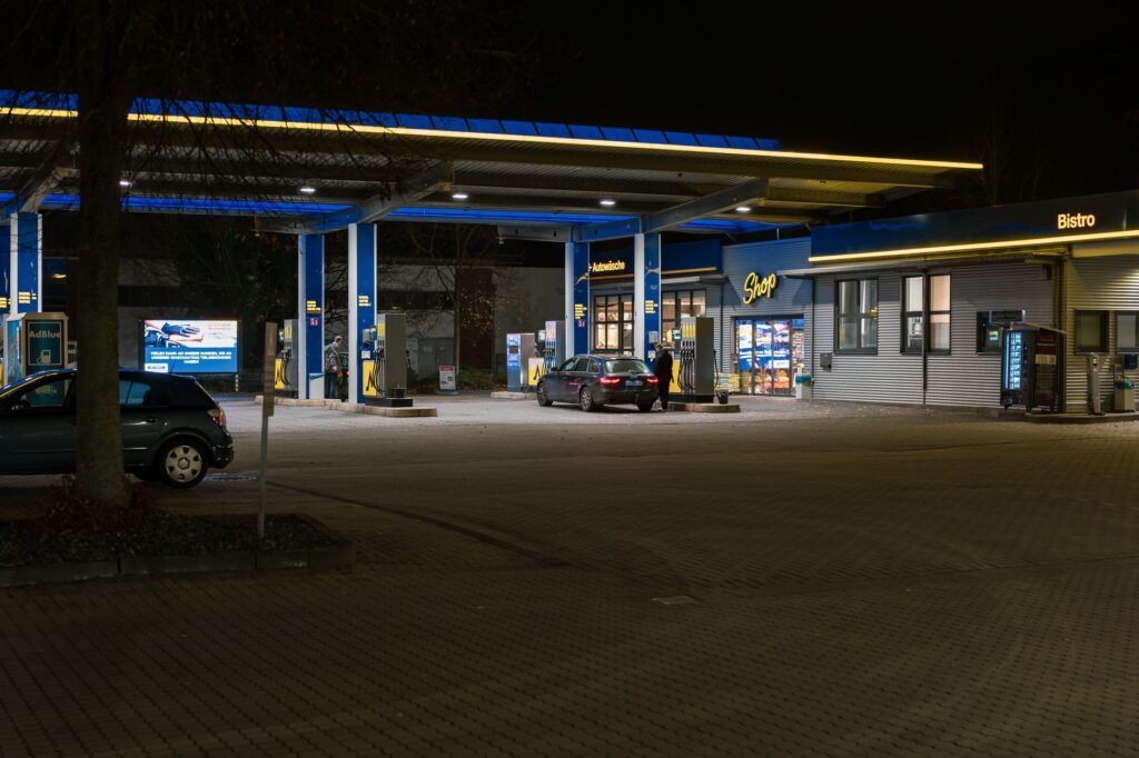 A well-lit gas station at night featuring cars and a bistro, creating a lively urban scene.