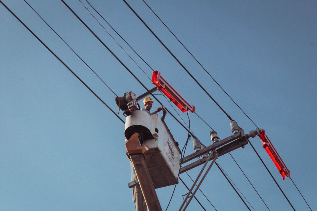 Electrician in a lift repairing overhead power lines on a clear day.