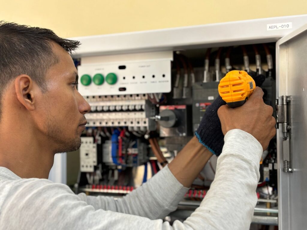 Skilled electrician using a drill to repair electrical equipment indoors. Focus on precision and safety.